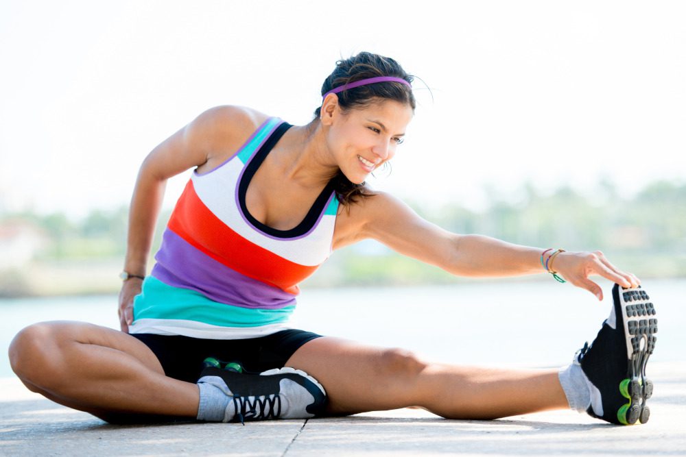 Fit woman doing stretching exercises outdoors and smiling.